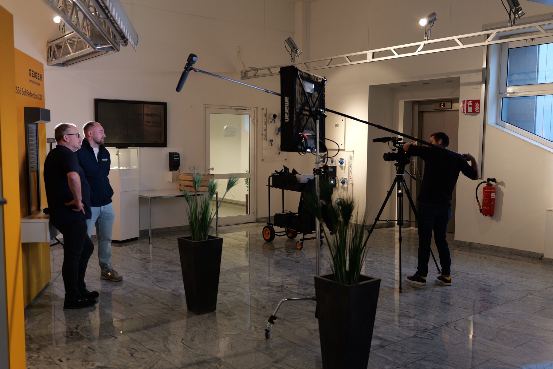 Filmteam dreht zwei Personen vor einem Bildschirm in einem Bürogebäude.